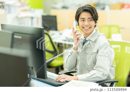オフィスで電話をする作業服の若い男性 オフィスで電話をする作業服の若い男性 113589994