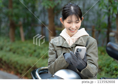 バイクに乗ってスマホを見る女性 113592608