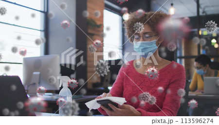 Image of covid 19 cells over woman in office disinfecting smartphone, wearing face mask Image of covid 19 cells over woman in office disinfecting smartphone, wearing face mask 113596274