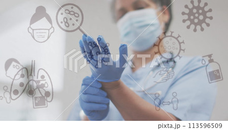 Image of covid 19 icons over female doctor putting gloves on wearing face mask 113596509