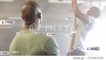Image of social media notifications over diverse male trainer and man climbing rope at gym 113597144