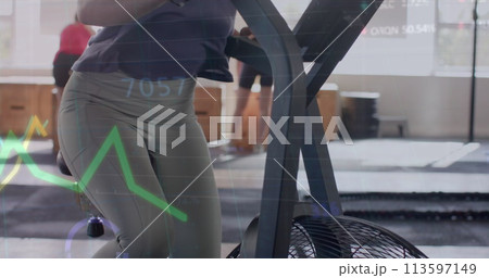 Image of data on graph over caucasian woman cross training on elliptical at gym 113597149