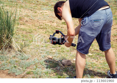 Young adult man shooting video on camera with handheld electronic stabilizer on nature in mountains in summer. Young adult man shooting video on camera with handheld electronic stabilizer on nature in mountains in summer. 113601960