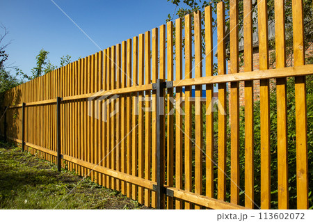 Close-up of a new wooden picket fence in the backyard of a country house, a sunny summer day Close-up of a new wooden picket fence in the backyard of a country house, a sunny summer day 113602072