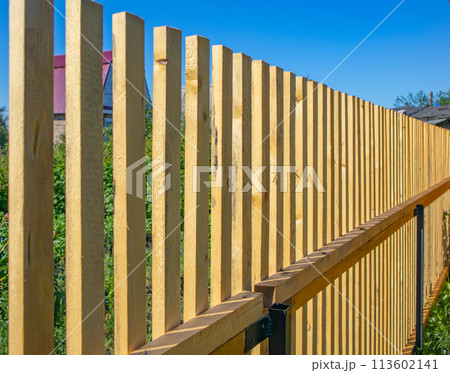Close-up of a new wooden picket fence in the backyard of a country house, a sunny summer day 113602141