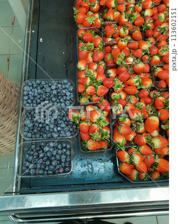 Lots of blueberries and strawberries in containers on the counter in the store, close-up, vertical Lots of blueberries and strawberries in containers on the counter in the store, close-up, vertical 113602151