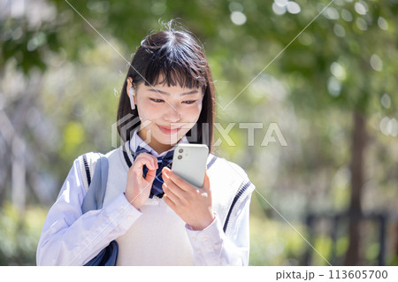 イヤホンを付けてスマホを見ている女子高校生 113605700