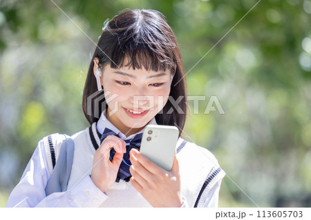 イヤホンを付けてスマホを見ている女子高校生 113605703