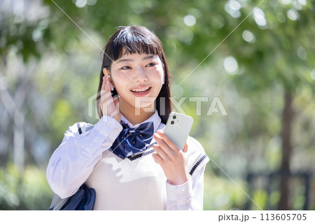 イヤホンを付けてスマホを見ている女子高校生 113605705