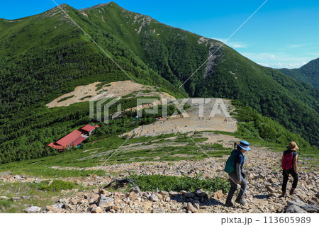 常念岳の登山道を歩く女性登山者2人と常念小屋と横通岳 113605989