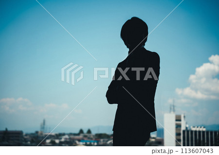 オフィスで腕組みしているスーツ姿の若い男性ビジネスマンのシルエット（悩む・考える・真剣） 113607043