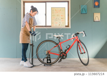 自宅の車庫でロードバイクのタイヤに空気を入れる若いアジア人女性 113607214