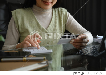 Cropped shot young woman holding credit card and calculating expenses at home 113608188
