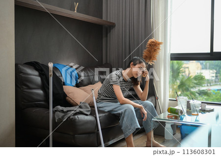 Young housewife sitting on sofa with cleaning tools feeling tired after doing housework Young housewife sitting on sofa with cleaning tools feeling tired after doing housework 113608301