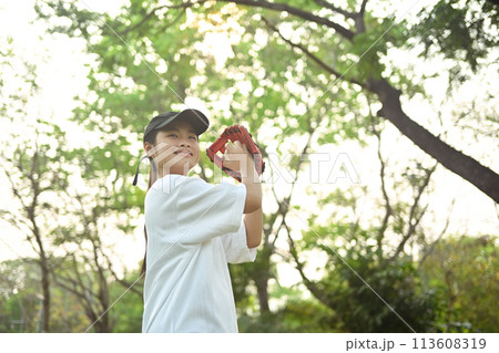 Joyful asian girl in leather glove playing baseball on green grassy lawn during summer day Joyful asian girl in leather glove playing baseball on green grassy lawn during summer day 113608319