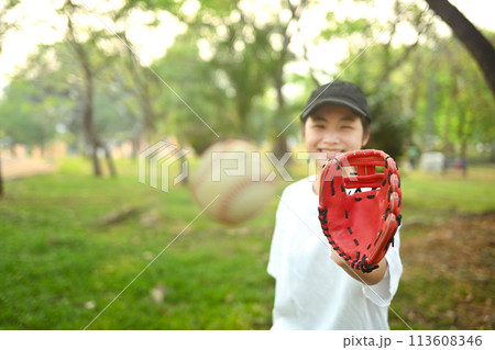 Joyful asian girl in leather glove playing baseball on green grassy lawn during summer day 113608346
