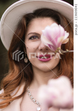 Woman holds magnolia flowers, surrounded by blossoming trees. Captured during spring, showcasing natural beauty and seasonal change. 113609041