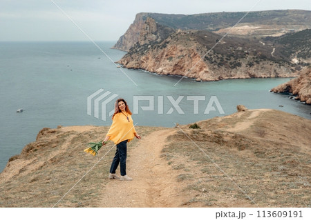 A woman is walking on a path near the ocean. She is carrying a bouquet of flowers. A woman is walking on a path near the ocean. She is carrying a bouquet of flowers. 113609191