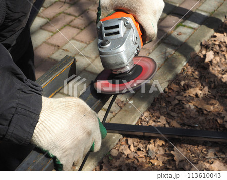 A worker processes metal with an angle grinder on a construction site. The concept of locksmith work, processing of metal products. A worker processes metal with an angle grinder on a construction site. The concept of locksmith work, processing of metal products. 113610043