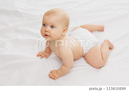 Serene, cute baby in diaper, rests on textured white fabric on bed embodying the calmness of early childhood. 113610899