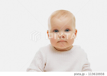 Portrait of cute, charming little baby, kid in dressed in white clothes looking at camera against white studio background. 113610938
