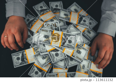 View from above. On a black background, a man holds his hands on either side of a stack of dollars with bitcoins on top. A trader made a large amount of money on a cryptocurrency exchange. View from above. On a black background, a man holds his hands on either side of a stack of dollars with bitcoins on top. A trader made a large amount of money on a cryptocurrency exchange. 113611132