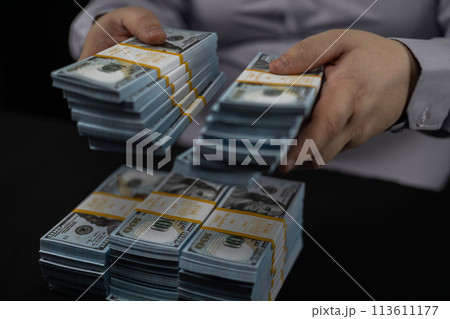 Folding money into piles on a black background. Close-up. A man carefully puts money in piles on a black background. A lot of money in packed bundles. 113611177
