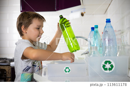 A boy enthusiastically puts plastic bottles into boxes separately from caps for recycling. Sorting plastic waste for recycling. The boy cares about preserving nature by sending plastic for recycling. 113611178