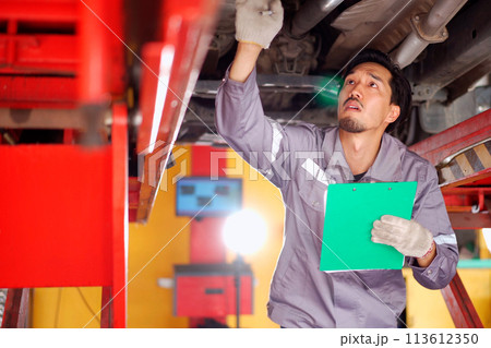 Professional Asian car technician or repairman inspecting the suspension system under the car. Repairman working in garage. Professional Asian car technician or repairman inspecting the suspension system under the car. Repairman working in garage. 113612350