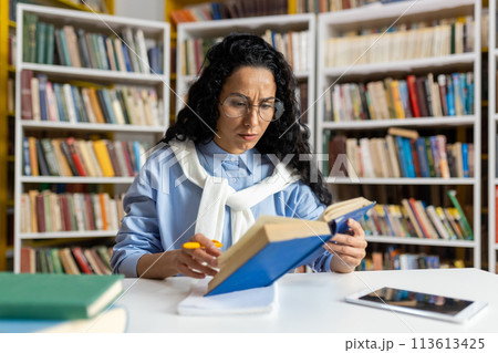 A dedicated student engrossed in reading a book surrounded by a vast collection of literature in a well-stocked library. 113613425