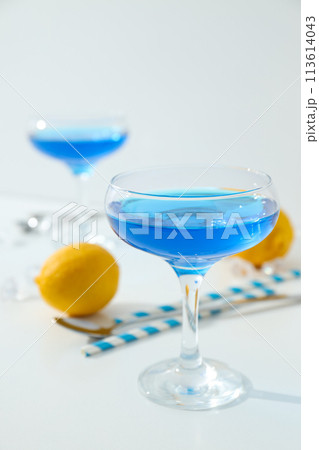 Blue cocktail in glass, whole lemon, straws and ice cubes on white background 113614043