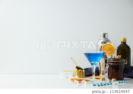 Blue cocktail in glass, oranges slices, bottles and ice cubes on white background, space for text 113614047