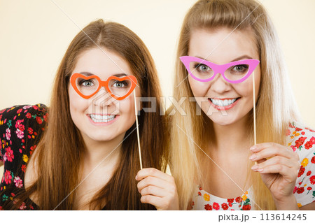 Two happy women holding fake eyeglasses on stick 113614245