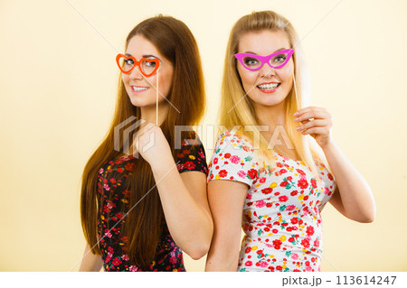 Two happy women holding fake eyeglasses on stick 113614247