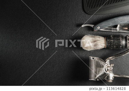 On a black surface are old barber tools.Two vintage manual hair clipper, comb, razor, shaving brush. black monochrome. Horizontal orientation. Top view, flat lay. copy space 113614828