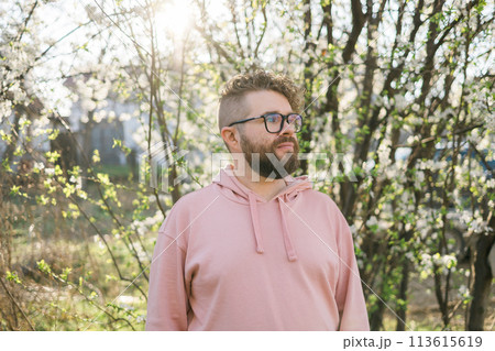 Male bearded man standing under branches with flowers of blooming almond or cherry tree in spring garden. Spring blossom. Copy space 113615619