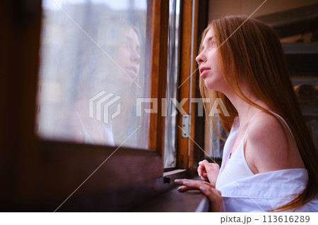 Young redhead Woman in white shirt Looks Out The Window on the balcony Deep In Thought red hairs ginger girl general plane Young redhead Woman in white shirt Looks Out The Window on the balcony Deep In Thought red hairs ginger girl general plane 113616289