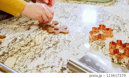 Using various festive cookie cutters, we're cutting out charming gingerbread cookies from the rolled dough on the sleek marble counter, bringing holiday cheer to the modern kitchen. Using various festive cookie cutters, we're cutting out charming gingerbread cookies from the rolled dough on the sleek marble counter, bringing holiday cheer to the modern kitchen. 113617379