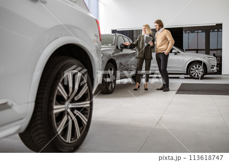 Caucasian male customer in vehicle showroom, female person selling transport. 113618747