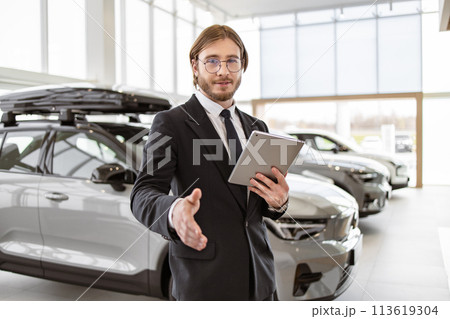 Bearded manager shaking hand with buyer on background of rows of crossovers. Bearded manager shaking hand with buyer on background of rows of crossovers. 113619304