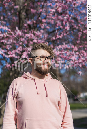 Man allergic enjoying after treatment from seasonal allergy at spring. Portrait of happy bearded man smiling in front of blossom tree at springtime. Spring blooming and allergy concept. Copy space Man allergic enjoying after treatment from seasonal allergy at spring. Portrait of happy bearded man smiling in front of blossom tree at springtime. Spring blooming and allergy concept. Copy space 113619996