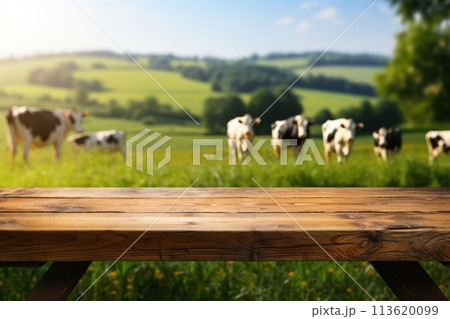 Empty wooden tabletop and blurred rural background of cows on green field and meadow with grass. Space for design your product. 113620099