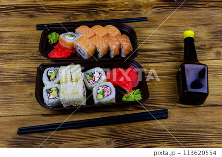 Set of sushi rolls in plastic boxes, soy sauce and chopsticks on wooden table. Sushi for take away or delivery of sushi in plastic containers Set of sushi rolls in plastic boxes, soy sauce and chopsticks on wooden table. Sushi for take away or delivery of sushi in plastic containers 113620554