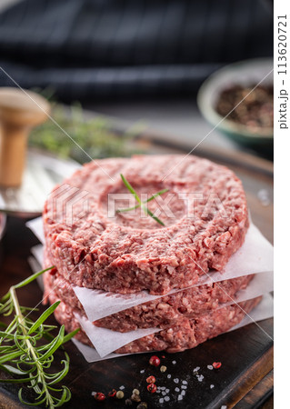 Fresh raw ground beef patties with rosemary salt and pepper made in a meat form on a cutting board Fresh raw ground beef patties with rosemary salt and pepper made in a meat form on a cutting board 113620721