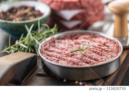 Fresh raw ground beef patties with rosemary salt and pepper made in a meat form on a cutting board 113620730