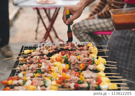 A man grilling pork and barbecue in dinner party. Food, people and family time concept. A man grilling pork and barbecue in dinner party. Food, people and family time concept. 113622205