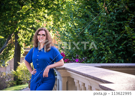 Beautiful young smiling woman in sunglasses in city park at summer day wearing dress and looking to the camera 113622995