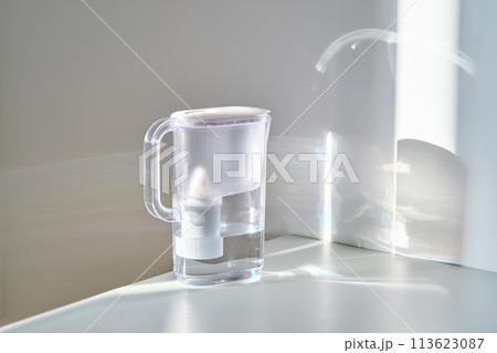 A jug with a water filter in the sun on the table. 113623087