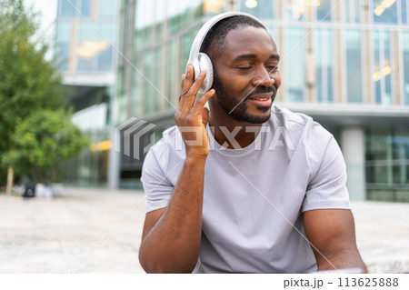 Music song concept. Good start day. Happy African American man listening modern hit on street in city. Person guy wearing headphones enjoy listening favorite music outdoor. People lifestyle joy 113625888