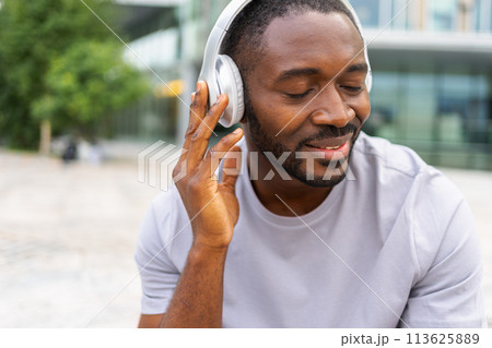 Music song concept. Good start day. Happy African American man listening modern hit on street in city. Person guy wearing headphones enjoy listening favorite music outdoor. People lifestyle joy 113625889